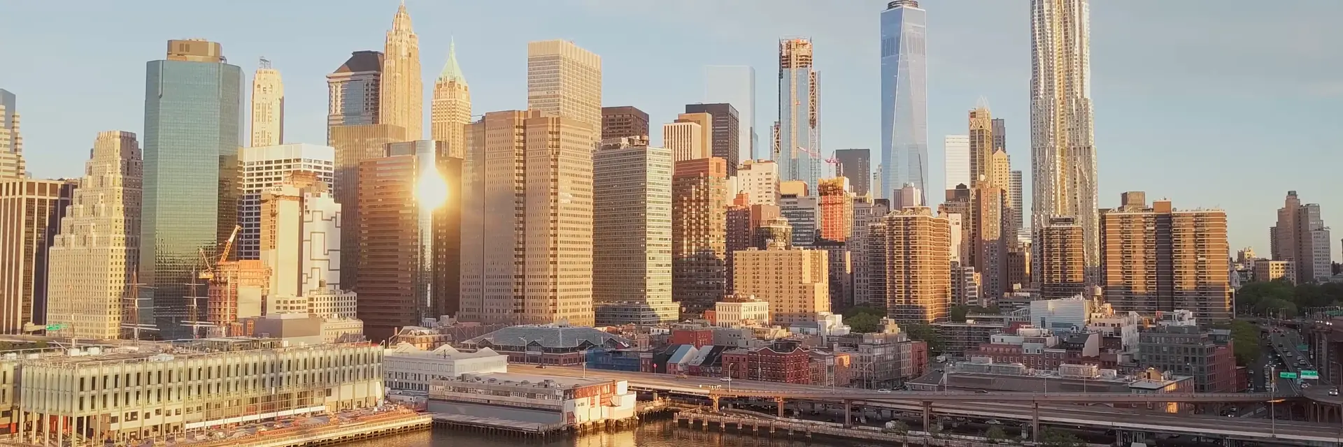 Lower Manhattan at golden hour, seen from the air across the East River.